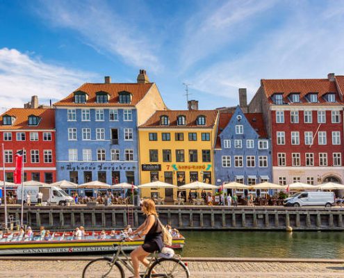 A photo of a woman biking in Nyhavn, Copenhagen during a sunny day | Copenhagen Private Walking Tour | 6 Hours | Amitylux Tours | Guided City Tours | VIP & Luxury Experiences