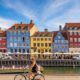 A photo of a woman biking in Nyhavn, Copenhagen during a sunny day | Copenhagen Private Walking Tour | 6 Hours| Amitylux Tours | Scandinavian Guided Tours | VIP & Luxury Experiences in the Nordics