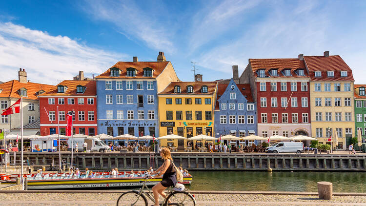 A photo of a woman biking in Nyhavn, Copenhagen during a sunny day | Copenhagen Private Walking Tour | 6 Hours | Amitylux Tours | Guided City Tours | VIP & Luxury Experiences