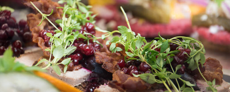 A photo of an open face sandwich with meat and green leaves and berries | The Best 5 Traditional Dishes in Denmark | Amitylux Tours | Scandinavian Guided Tours | VIP & Luxury Experiences in the Nordics