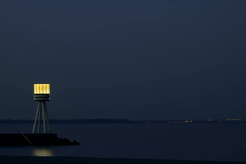 A photo of Bellevue beach at night with a small lighthouse lighting up | Most Beautiful Beaches Across Copenhagen | Amitylux Tours | Scandinavian Guided Tours | VIP & Luxury Experiences in the Nordics