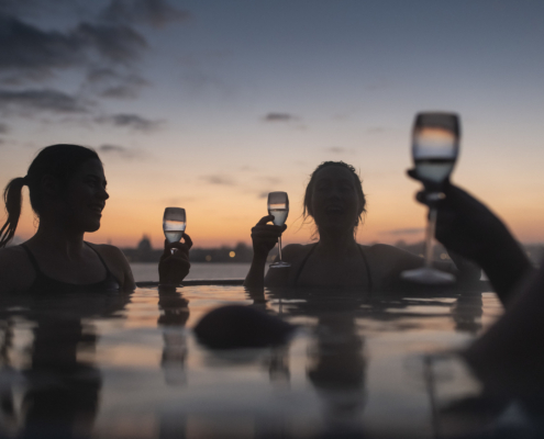 An outside photo of a jacuzzi at CopenHot with people holding champagne glasses and drinking champagne | Photo of people in a spa | The Best 5 Spas in Copenhagen | Amitylux Tours | Guided City Tours | VIP & Luxury Experiences