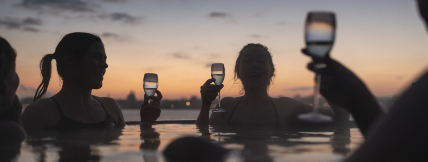 An outside photo of a jacuzzi at CopenHot with people holding champagne glasses and drinking champagne | Photo of people in a spa | The Best 5 Spas in Copenhagen | Amitylux Tours | Scandinavian Guided Tours | VIP & Luxury Experiences in the Nordics