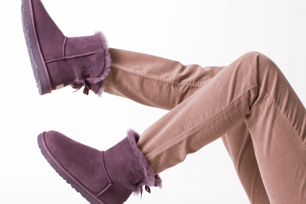 A photo of a woman's two legs from the thigh down, wearing brown jeans and purple winter boots