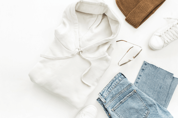 A photo in a white background showing white shoes, a white blouse, a brown cap, and bluejeans