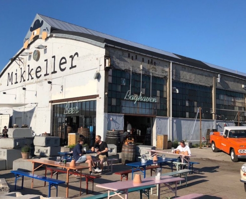 An outside photo of Mikkeller showing people sitting outside on benches drinking beer | The Best Beer Bars in Copenhagen: Our Top 4 Favorite | Amitylux Tours | Guided City Tours | VIP & Luxury Experiences