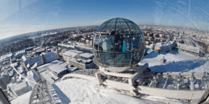 An outside photo of Avicii Arena at the top showing people inside the round teleporting sphere in the snowy top of tue building | Stockholm (Part 2): A Must See List of Unique Sites | Amitylux Tours | Guided City Tours | VIP & Luxury Experiences