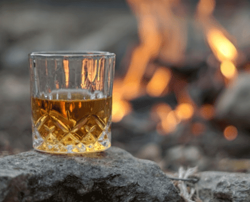 a glass of whisky on a rock next to a camp fire
